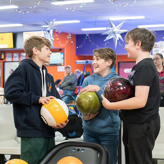 Three boys laughing together while bowling at Sunset Superbowl