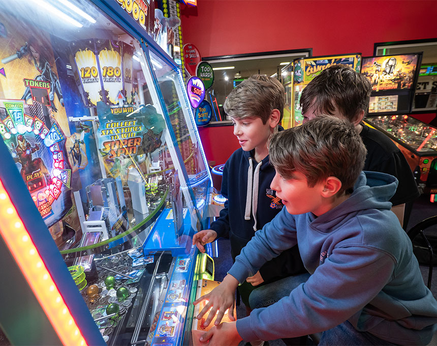 Three boys playing arcade games together at Sunset Superbowl